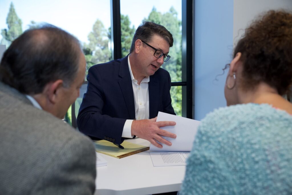 Patent attorney in Irvine, California, meets with two clients at a desk to discuss patent application.